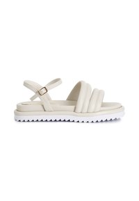 Beige platform sandaalit, joissa on kolme paksua, pyöristettyä hihnaa ja solkikiinnitys. Pohja on valkoinen ja siinä on sahalaitareuna paremman pidon saavuttamiseksi.