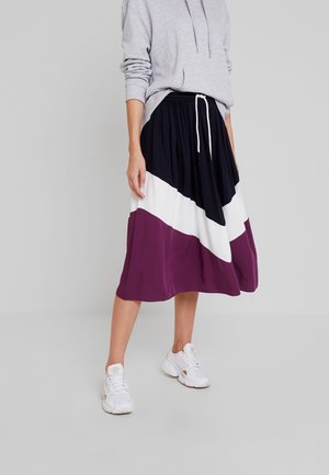Persoon die een color-block midi rok draagt in zwart, wit en paars, gecombineerd met witte sneakers en een lichtgrijze hoodie.