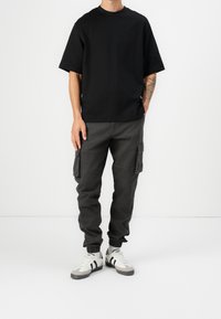 Zwarte korte mouwen t-shirt, grijze cargobroek met zijzakken, en witte sneakers met grijze accenten, met een ronde hals en een comfortabele pasvorm.