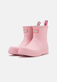 Stivali da pioggia in gomma rosa con una texture liscia, punta arrotondata e linguette a strisce sulla parte superiore. Presentano il logo "HUNTER" su entrambi i lati.