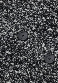 Dzianinowa tkanina w czerni i bieli z teksturowanym, grubym wzorem. Posiada dwa czarne guziki z logo "ELEMENT".
