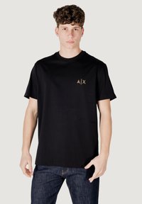 Zwarte katoenen t-shirt met een ronde halslijn en korte mouwen. Het heeft een klein gouden logo op de borst en een ontspannen pasvorm.