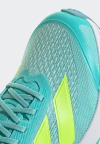 Teal athletic shoe with textured mesh upper, contrasting neon yellow accents, and a rubber sole. Features padded tongue and laces.