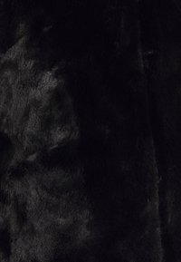 Czarna tkanina z sztucznego futra o miękkiej fakturze, charakteryzująca się gęstym włosiem i delikatnym połyskiem, z nieregularnymi wzorami w całej powierzchni.