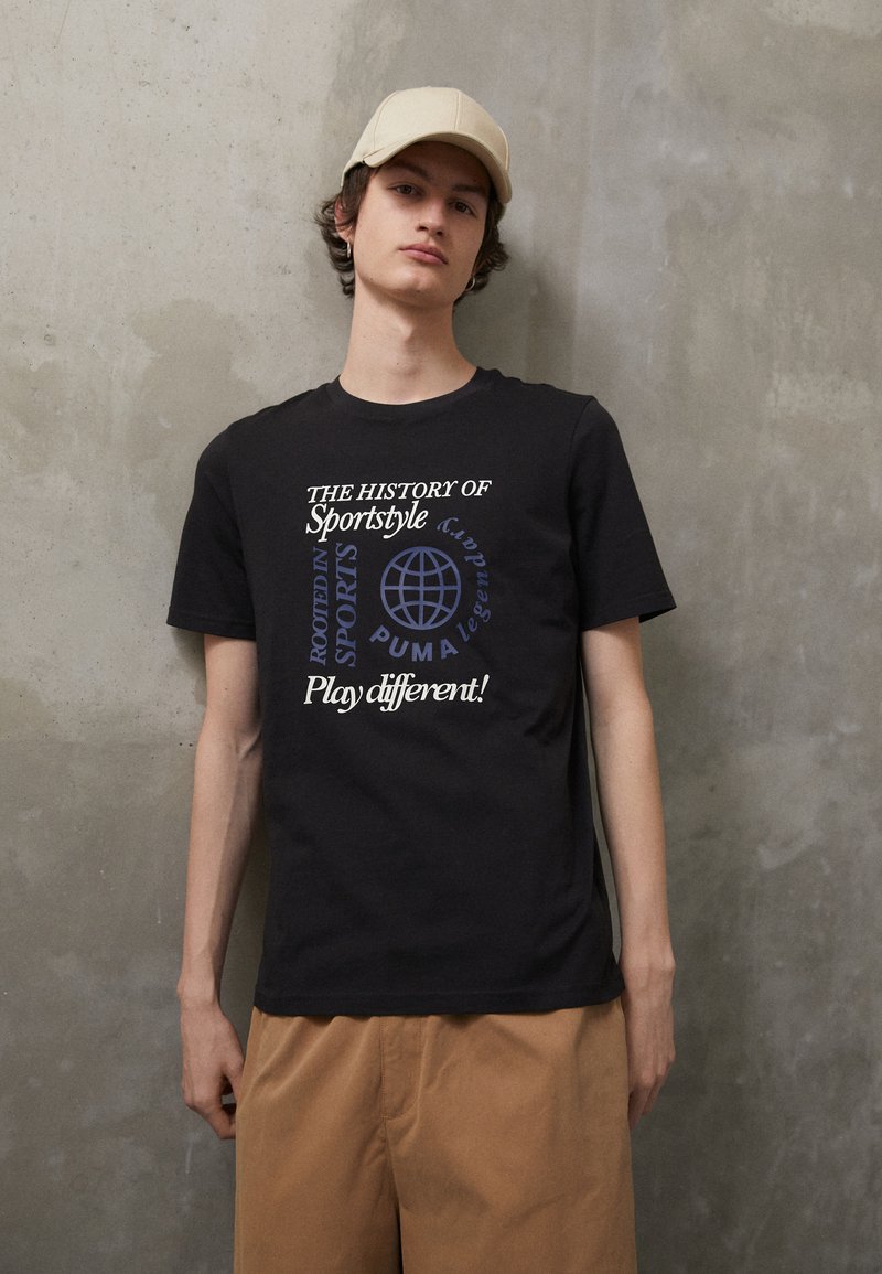 Zwarte katoenen T-shirt met meerkleurige tekstgraphics, korte mouwen en een relaxte pasvorm. Gecombineerd met beige shorts voor een neutrale achtergrond.