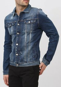 Veste en denim bleu foncé avec des accents usés, fermeture à boutons, deux poches poitrine et un col classique. Style ajusté avec des manches longues.