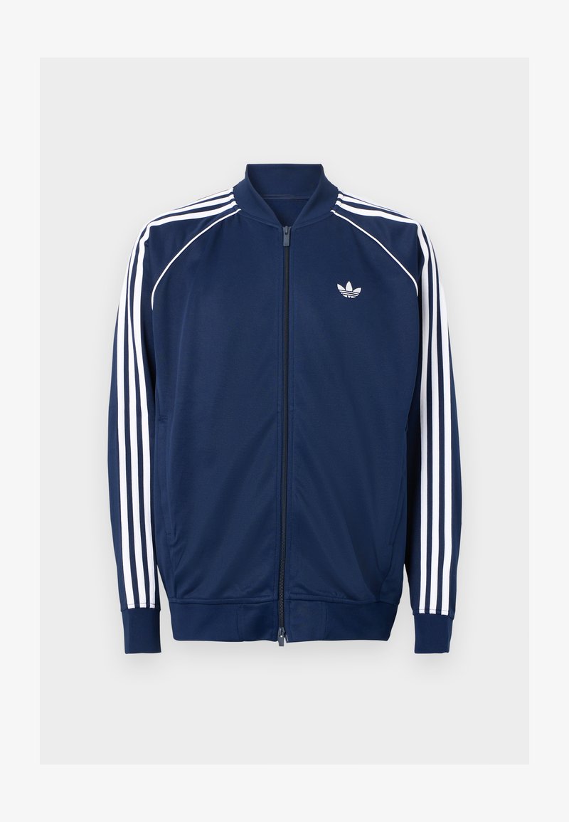 Veste zippée bleu marine en tissu lisse. Caractéristiques d'un design à trois rayures blanches sur les manches et d'un logo blanc sur la poitrine.