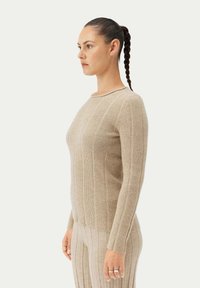 Beige ribbad stickad tröja med långa ärmar och rund halsringning, med vertikala ränder och en mjuk, texturerad yta.