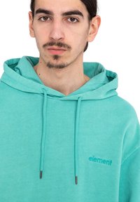 La sudadera turquesa cuenta con un cordón, un bolsillo frontal y un logo "element" bordado en el pecho. Fabricada con un tejido suave y texturizado, presenta un corte relajado.