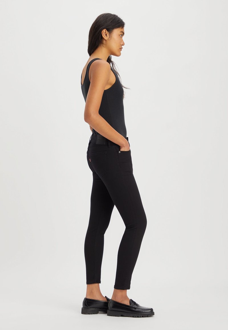 Schwarzes Tanktop und schwarze Skinny-Jeans, die an einem Modell präsentiert werden, mit glatter Textur, taillierter Passform und minimalistischen Stil.
