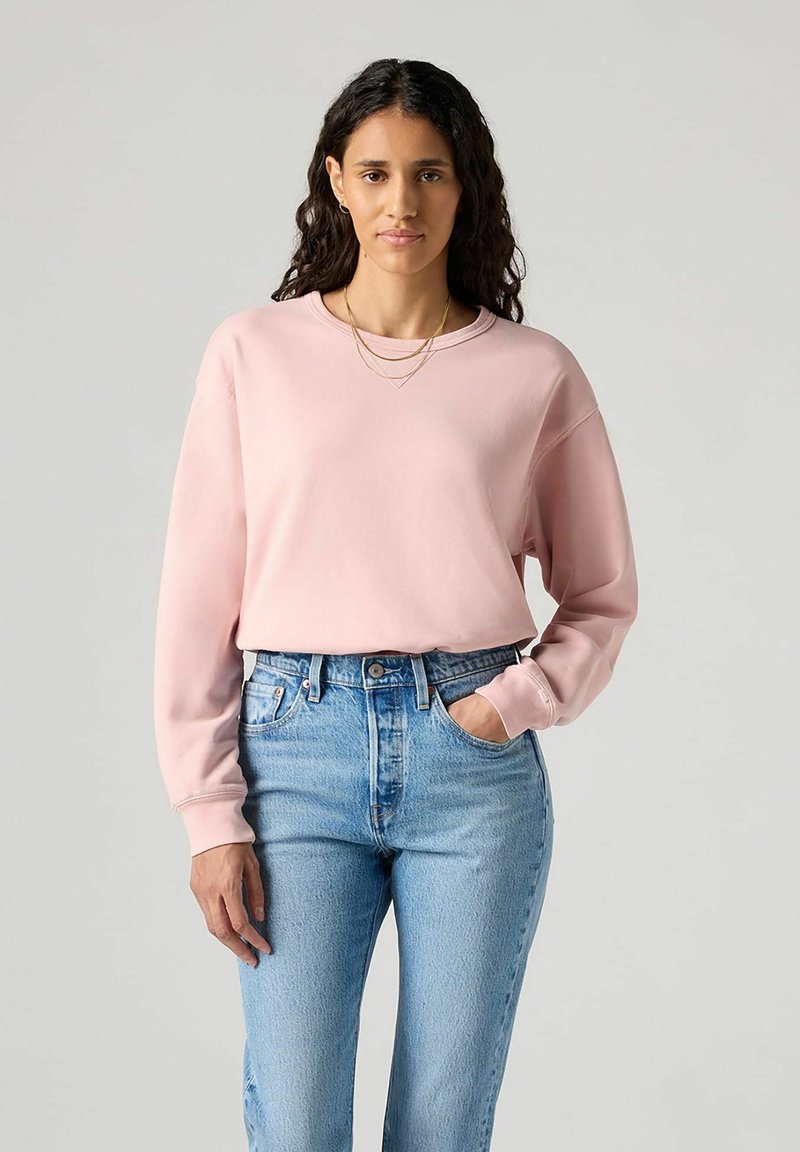 Sweat-shirt rose clair à manches longues, col rond et coupe décontractée, associé à un jean bleu taille haute.