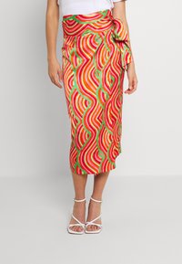 Jupe midi colorée avec un motif ondulé en rouge, orange et vert, dotée d'un détail de taille nouée. Le tissu semble lisse et léger.