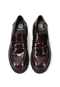 Mocassini in pelle verniciata bordeaux con una fascia ampia, punta arrotondata e una suola spessa nera. Logo sulla soletta. Finitura liscia e lucida.