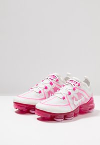 Scarpe da ginnastica bianche con dettagli rosa, dotate di tomaia in rete, un motivo a zigzag e una suola air-cushion distintiva di colore rosa trasparente.