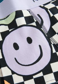 Tessuto di cotone multicolore con un grande sorriso viola su uno sfondo a scacchi bianco e nero, arricchito da accenti arancioni e verdi.