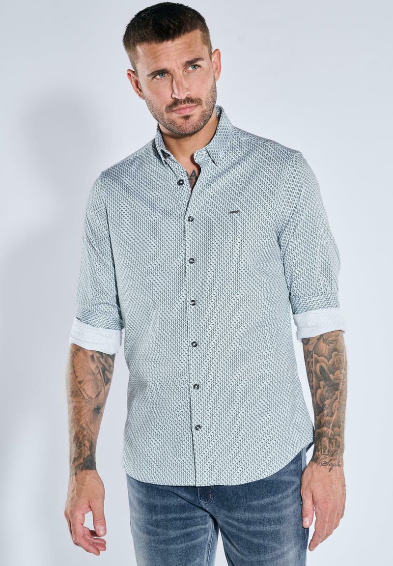Hellblau gemustertes Hemd mit Knöpfen und Kragen, hochgesteckten Ärmeln und dunklen Knöpfen, kombiniert mit blauen Jeans. Verfügt über ein dezentes Logodetail.
