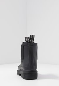 Bottines en caoutchouc noires avec des panneaux élastiques sur les côtés, semelle texturée et languettes de traction à l'arrière. Design minimaliste avec une marque sur le côté.