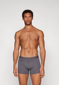 Szürke pamut boxeralsó márkás elasztikus derékpánttal, testhezálló kialakítással, látható minták nélkül. A modell semleges háttér előtt pózol.