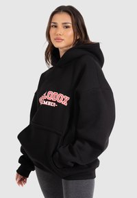 Černá oversized mikina s velkou přední kapsou, na hrudi s červeným nápisem. Vyrobena z měkké tkaniny s žebrovanými manžetami a lemem.