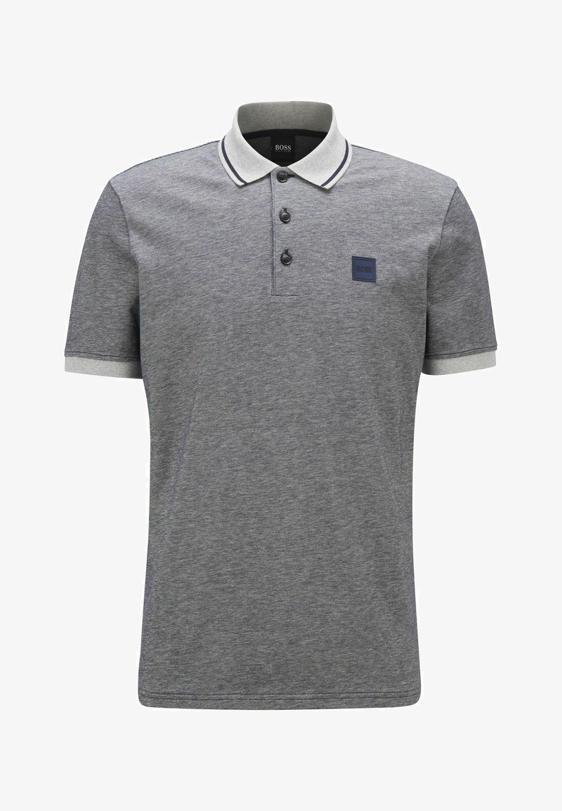 Polo gris avec un tissu texturé, trois boutons noirs, un col et des manches rayés blancs, et un patch logo bleu marine sur la poitrine.