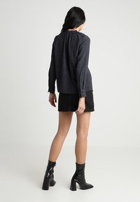 Dark patterned blouse with long sleeves, gathered neckline, paired with a black denim skirt and shiny black ankle boots.
