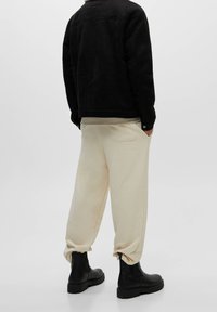 Sort oversized jakke, beige sweatpants med en baglomme og sorte ankelstøvler med robuste såler. Glat stof med afslappet pasform.