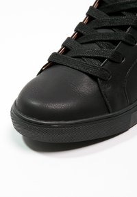 Černé kožené tenisky s texturovaným svrškem, kulatou špičkou a plochou gumovou podešví. Obsahují černé tkaničky a minimální prošití.