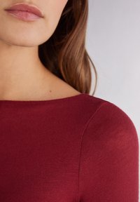 Bordeaux langemouwen top, met een ronde halslijn en een gladde, zachte textuur, met minimale naden en een getailleerde silhoutte.
