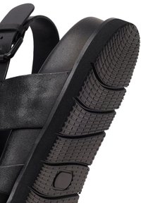 Czarna skórzana sandałka z regulowanym paskiem na klamrę oraz grubą gumową podeszwą z głębokim, teksturowanym bieżnikiem zapewniającym lepszą przyczepność i wygodę.