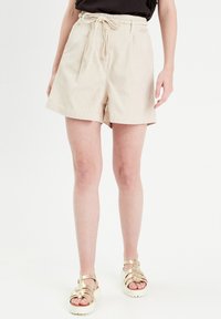 Shorts en coton beige avec une coupe décontractée, ceinture élastique et fermeture à cordon. Comprend des poches latérales et un ourlet plat.