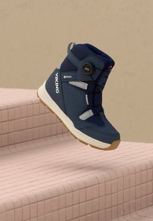 Blue Viking Gore-Tex hiking boot with BOA lacing system suspended above pink tiled stairs against beige background.