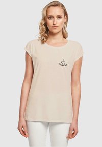 Jasno beżowy t-shirt wykonany z miękkiego materiału, z krótkimi rękawami i zaokrąglonym dekoltem; na przodzie znajduje się logo czarnej filiżanki kawy.