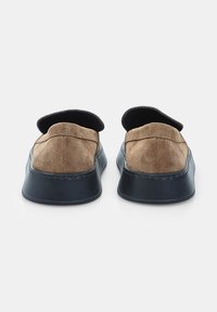 Bruine suède instapschoenen met een ronde neus, zwarte rubberen zool en zichtbare stiksels langs de rand.