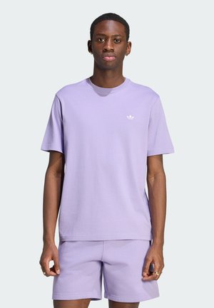 Jeune homme portant un t-shirt Adidas violet clair et un short assorti, debout devant un fond uni clair, regardant droit devant.