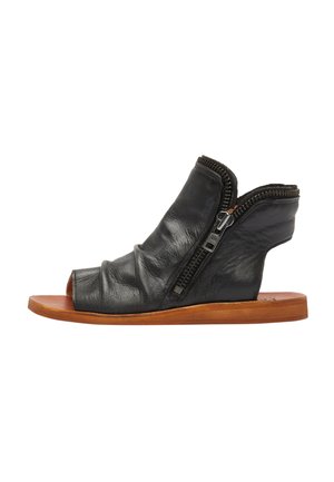 Sandali aperti neri in pelle con texture increspata, zip laterali e una soletta in legno minimalista. Presentano un design asimmetrico.