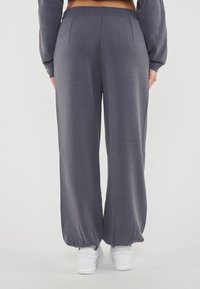 Pantaloni larghi grigi realizzati in tessuto morbido con una cintura elasticizzata. Presentano due tasche posteriori e sono abbinati a sneakers bianche.