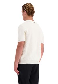 Kortemouwen polo trui in crème, met een textuur breiwerk, een effen witte kraag en een geribde zoom. Achterstevoren gedragen, met minimale details.