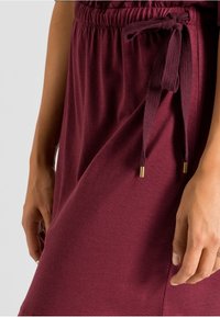Maroon dress with an elastic waistband and a tied drawstring. Features a smooth texture and gold-tone accents on the drawstring ends.