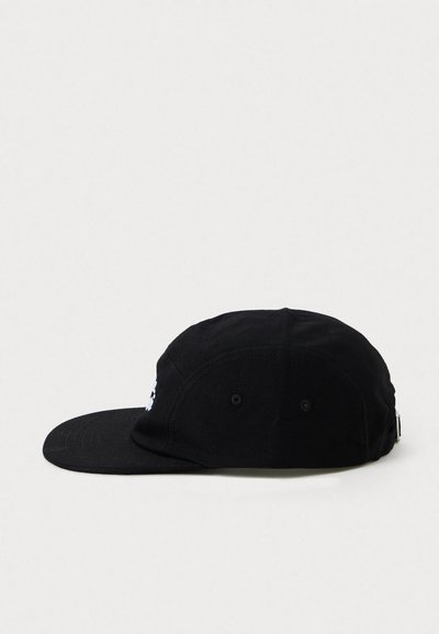 Gorra negra con visera plana, hecha de tela, con un detalle de logo blanco en la parte frontal y orificios de ventilación a los lados.