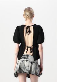 Top nero con maniche a sbuffo e scollatura profonda sul retro, legato con un nastro nero. Abbinato a una gonna di jeans grigia con orlo arruffato e motivo.