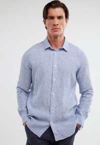 Camicia a maniche lunghe a righe blu e bianche con apertura a bottoni, colletto e texture morbida. Presenta due tasche frontali e una vestibilità rilassata.