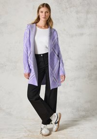Paarse gebreide cardigan met een textuur van een diamanten patroon, open voorkant, zakken, gecombineerd met zwarte broek en witte sneakers.