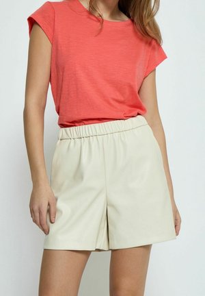 Koraliowy top z krótkim rękawem w zestawie z beżowymi szortami z elastycznym pasem. Szorty mają gładką fakturę i szeroki krój.