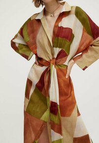 Robe chemise surdimensionnée colorée avec des motifs géométriques en orange, vert et crème. Confectionnée en tissu léger et ajustée avec un lien à l'avant.