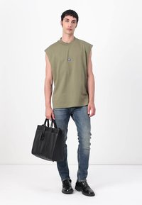 Camisa sin mangas verde, jeans de mezclilla azules, bolso estructurado negro, zapatos negros. Diseño sencillo con detalles mínimos y colores apagados.