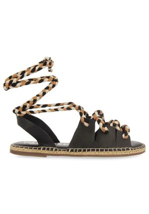 Sandal nera piatta con cinturini intrecciati marroni, neri e bianchi alla caviglia e dettagli intrecciati lungo il bordo della soletta.