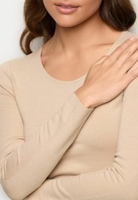 Beige Langarmshirt mit rundem Halsausschnitt, aus weichem, leichtem Stoff gefertigt, mit eng anliegenden Ärmeln und glatter Textur.