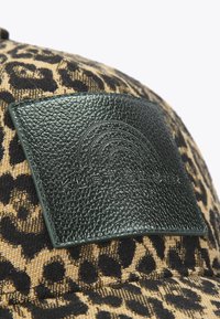 Pet met luipaardprint en een gestructureerd bruin-zwart patroon, met een groen geperst lederen plaatje met merknaam.