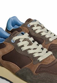 Baskets marron et grises en daim et en maille, avec des lacets beiges, des accents bleu clair et une semelle épaisse blanc cassé.