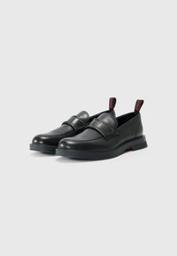 Sorte læder slip-on sko med en rund tå, et bredt bånd over forfoden og et kontrasterende rødt trækstykke ved hælen. Gummisål.